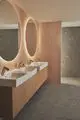 Waschtisch mit integrierten Sensorarmaturen und Seifenspender. Der Raum ist modern gestaltet mit Holz- und Steinoberflächen. Ideal Standard Produkte sind erkennbar.